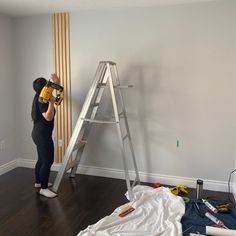 a woman is painting the walls in an empty room with ladders and paint supplies