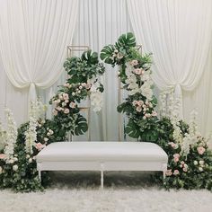 a white bench with flowers and greenery on it in front of a curtained window