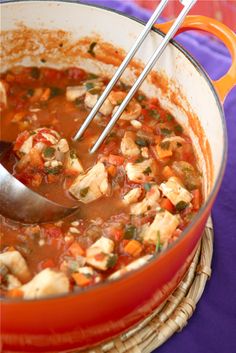 a large pot filled with soup on top of a purple cloth covered table next to a wooden spoon