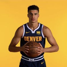 a man holding a basketball in his right hand and wearing a jersey with denver written on it