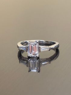 "Dekara Designs Custom Order Metal- 90% Platinum, 10% Iridium. Stones- GIA Certified Emerald Cut Diamond F-G Color VS1 Clarity 1.05-1.10 Carats. Two Tapered Baguette Diamonds, F-G Color VS1 Clarity 0.40 Carats. Ring Comes With GIA Certificate. Beautiful Handmade Art Deco Inspired Emerald Cut Diamond Three Stone Engagement Ring. The ring features a very fiery and elegantly set emerald cut diamond that is F-G in color with VS1 clarity in between four \"Eagle Claw\" prongs. There is a carat tapered Art Deco Emerald Ring With Baguette-cut Diamond, Art Deco Emerald Ring With Baguette Diamond, Luxury Octagon Diamond Ring With Baguette Diamonds, Timeless Diamond Cut Baguette Diamond Ring, Timeless Gia Certified Baguette Cut Diamond Ring, Elegant Gia Certified Baguette Cut Diamond Ring, Timeless Baguette Cut Gia Certified Diamond Ring, Timeless Baguette-cut Diamond Ring, Luxury Octagon Baguette Diamond Ring