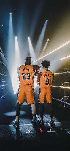 two basketball players standing in front of spotlights on a stage with their arms around each other