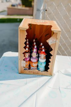 a wooden box with three bottles in it on top of a white cloth covered table