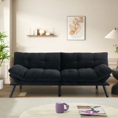 a living room with a black couch and coffee table next to potted plants on the floor