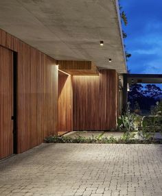 the entrance to a modern house with wooden doors and brick flooring at night time