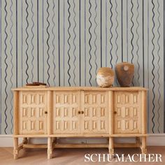 a sideboard with two vases on top of it in front of a striped wall