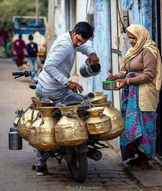 two people standing next to each other with pots on the back of a motorcycle