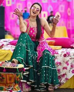 a woman sitting on top of a bed in a pink and green lehenga