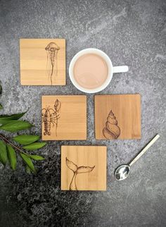 four coasters with drawings on them and a cup of coffee next to one that has a spoon in it