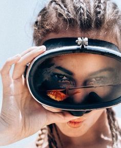 a woman looking through a mirror with fish in it's mouth and the reflection of her face