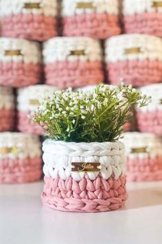 a pink and white crocheted basket with flowers in front of stacks of baskets