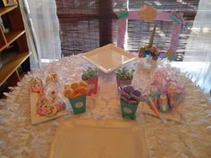 a table topped with plates and cups filled with food next to a window covered in sheer curtains