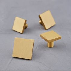 three square brass knobs on a gray surface, one is slightly open and the other has two small square knobs