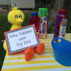 a stuffed animal sitting on top of a table next to bottles of water and a sign that says blow bubbles with big bird