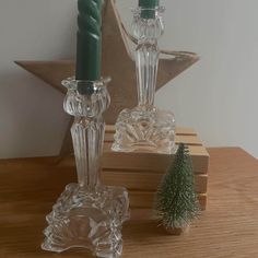 two glass candlesticks sitting on top of a wooden table next to a small christmas tree