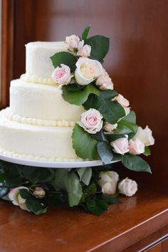 a three tiered wedding cake with pink roses on the top and green leaves around it