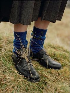 the legs and ankles of a person wearing black shoes with blue socks on them, standing in grass