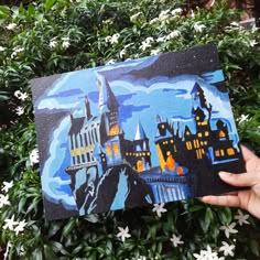 someone holding up a painting of hogwart's castle in front of some flowers