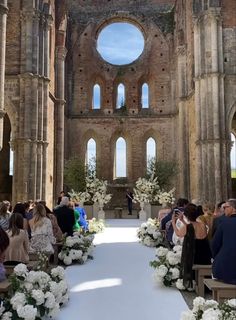 a wedding ceremony in an old building with white flowers and greenery on the aisle