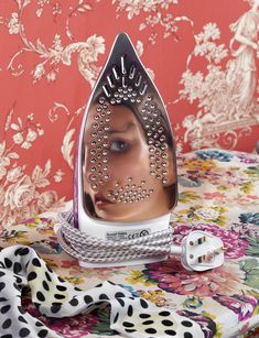 a woman's face is reflected in an iron on top of a floral tablecloth