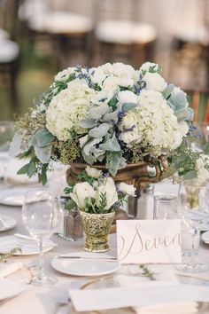 there is a vase with white flowers on the table and place cards in front of it