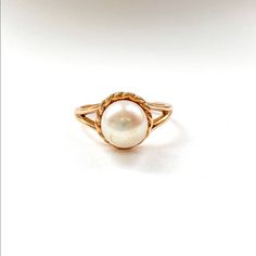 a gold ring with a white pearl in the center on a white background, close up