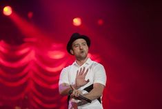 a man in white shirt and black hat on stage with his hands out to the side