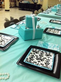 the table is set with blue and black plates, silverware, and gift boxes