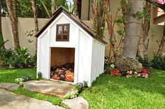 a small dog house in the middle of some grass and trees with flowers around it