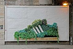 a bench covered in green plants on the side of a building