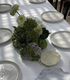 the table is set with white plates and green hydrangeas in vases on them