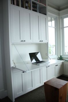 a laptop computer sitting on top of a desk in a room with white cupboards