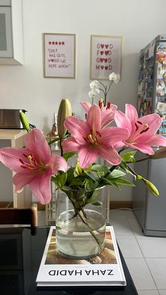 a glass vase with pink flowers in it sitting on a table next to a book