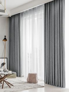 a living room filled with furniture and large windows covered in grey drapes next to a white rug