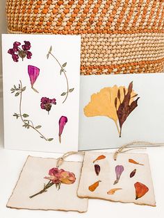 three cards with dried flowers on them are sitting next to a basket and some other items