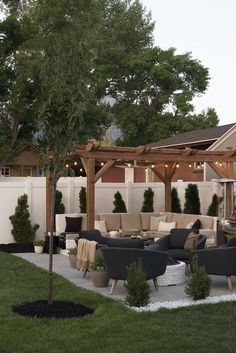 an outdoor living area with couches, chairs and trees in the back yard at dusk