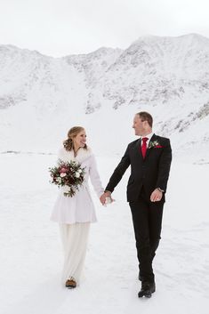 a bride and groom holding hands in the snow with mountains in the backgroud