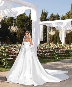 a woman in a white wedding dress standing under an arch with flowers and chandeliers