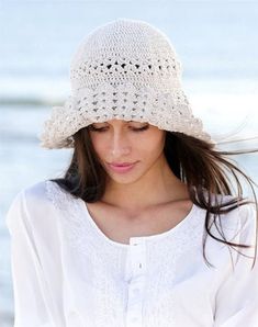 a woman wearing a white crochet hat on the beach looking down at her cell phone