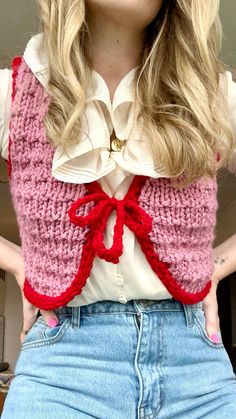 a woman with long blonde hair wearing a pink and red knitted vest over her shoulders