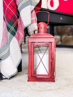 a red lantern sitting on the ground next to a person's leg and plaid blanket