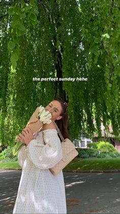 a woman standing under a tree holding a bunch of flowers in her hands and looking at the camera