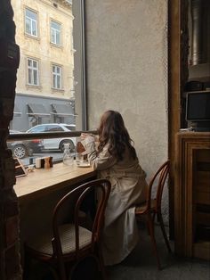 a woman sitting at a table in front of a window looking out on the street