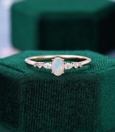 a white opal and diamond ring sitting on top of a green velvet box