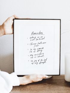 a person holding up a framed poem in front of a candle and some white candles