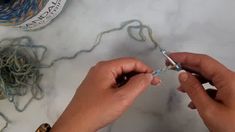 two hands are working with yarn on a marble counter top, while another hand is holding a crochet hook