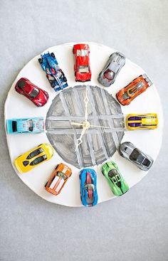 a clock made out of toy cars sitting on top of a white table with grey background