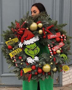 a woman holding a christmas wreath with the grin face on it and other decorations around her