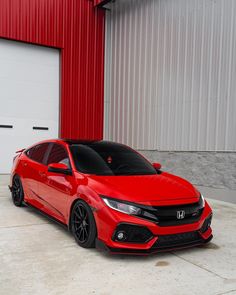 a red honda civic is parked in front of a garage with a red wall behind it