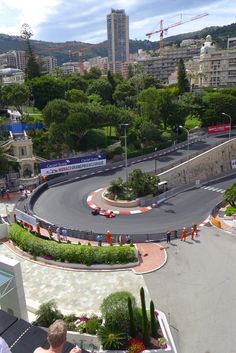 an aerial view of a race track with cars driving on it and buildings in the background